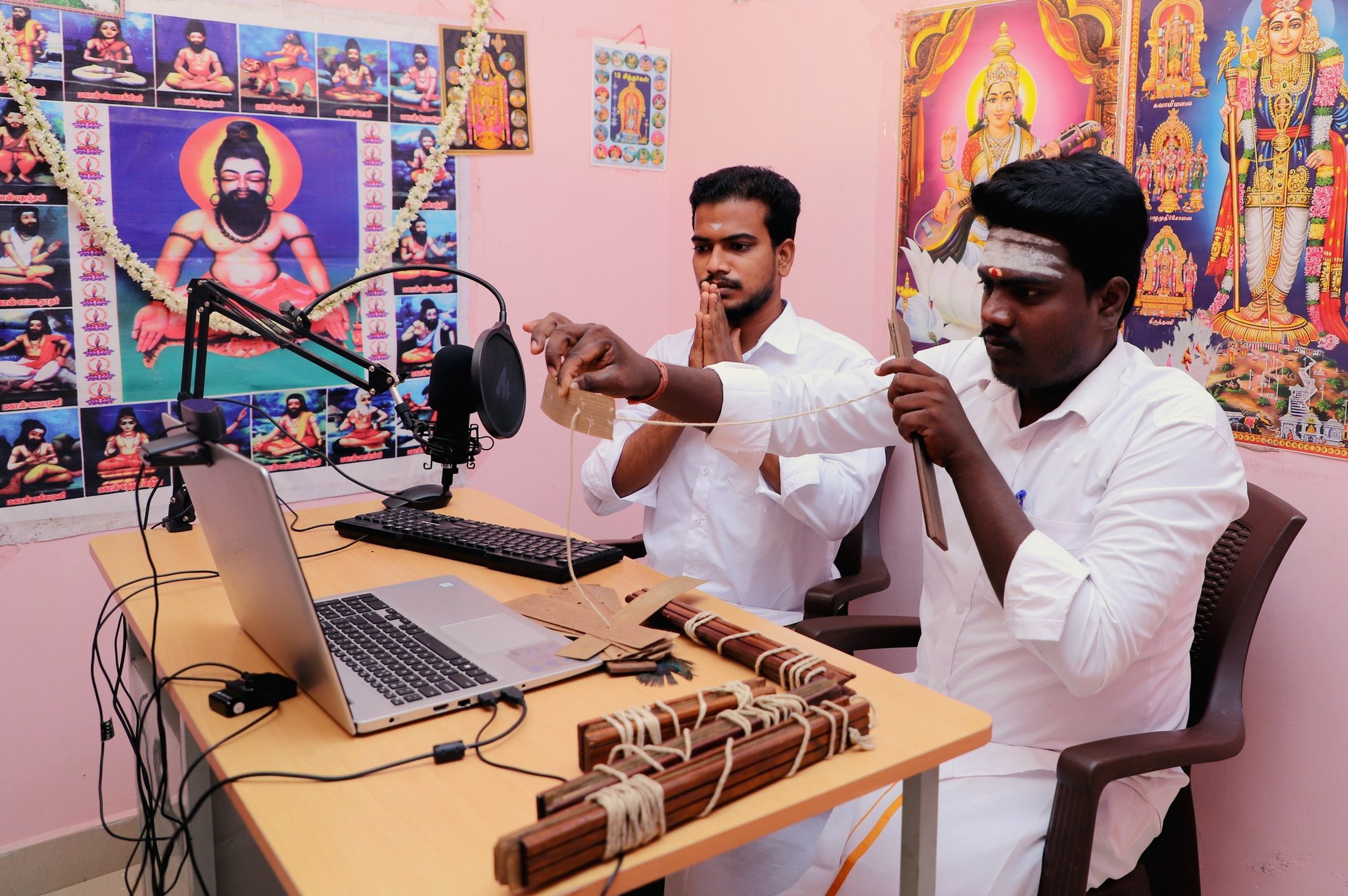 Two readers at the desk during a live reading, the leaf bundles and the laptop in front of them