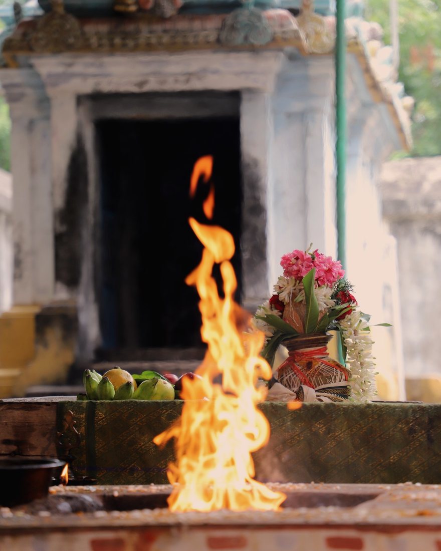 A tall flame rising from the homa fire, with flowers and offerings beside it