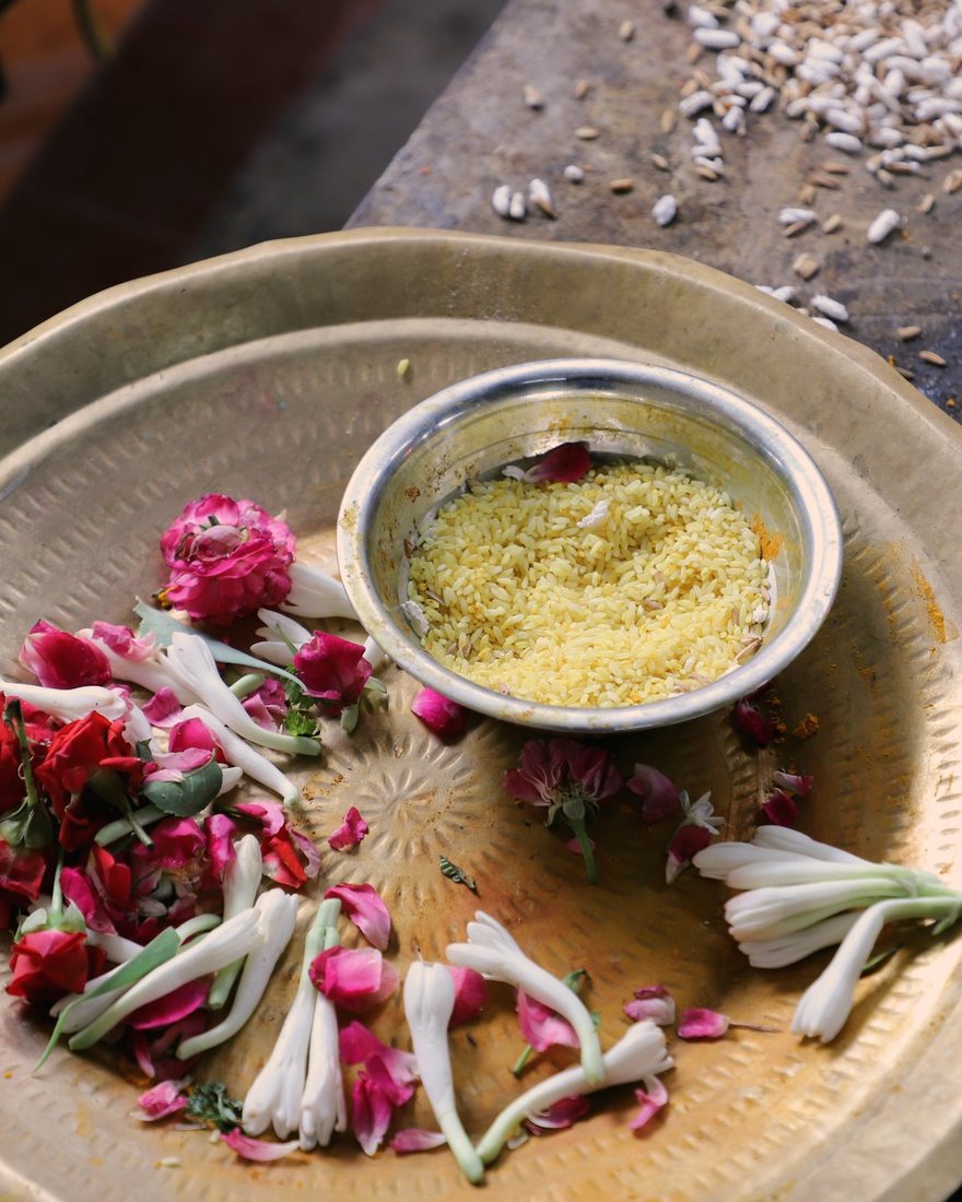 A brass offering plate seen from above, with rose petals, white flowers and ghee
